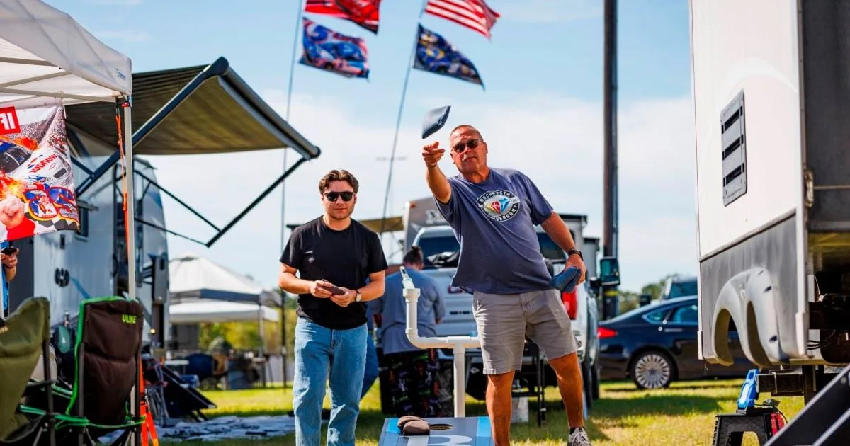 NASCAR fans playing cornhole beside RVs at a Charlotte Motor Speedway campground